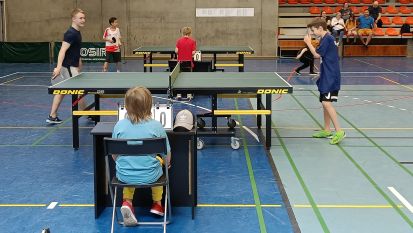 Kilka osób grających w sali sportowej w tenisa stołowego